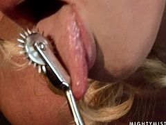 Perverse brunette mistress suspends a submissive curvy blond with her head looking down before she starts stroking her tits and the rest of the body with spiked metal roller in BDSM-involved sex video by 21 Sextury.