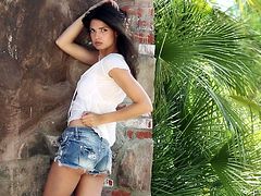 Sexy girl is wearing white top and jeans shorts. She takes teasing position posing in front of camera outdoor. She performs incredibly arousing outdoor erotic photoshoot.