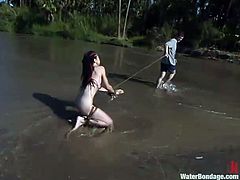 Brunette chick walks naked by the river being tied up. Then she lies in a dirt and gets whipped painfully by her master.