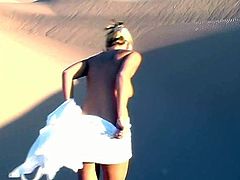A sweet girl in a white dress lies on sand. She shows her juicy boobs and booty. Later on she takes the dress off and walks around.