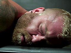 Time to enjoy hot bdsm threesome with Riley Mitchell. The muscular tattooed guy is bound by ropes and is lying on his stomach, while a man kisses and licks his feet, and another guy strokes, and sucks his dick